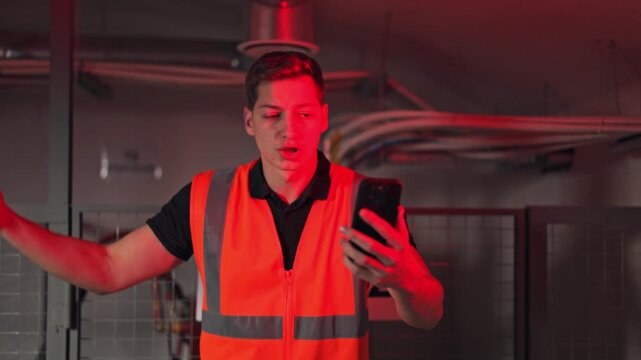 Worker wearing safety vest displays concern and confusion while viewing urgent red warning on smartphone screen. Communication and problem-solving actions indicated during system alert.
