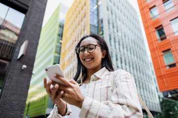 Smiling woman using smartphone outdoors in modern urban city
