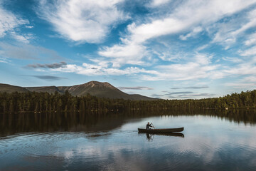 Woman paddles canoe alone across peaceful lake in Maine