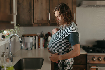 Father babywearing newborn in kitchen, nurturing and bonding