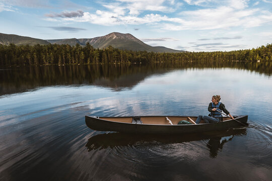 Woman paddles canoe alone on lake in Maine woods