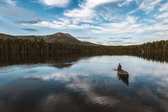 Female rows boat alone across beautiful pond in Maine