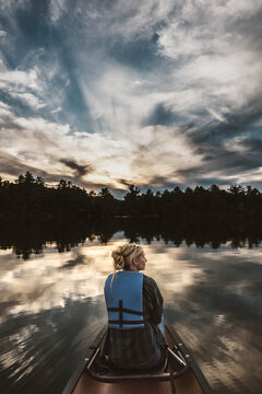 Woman sits in front of canoe on peaceful lake in Maine woods