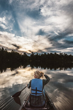 Woman paddles canoe across beautiful lake in Maine at sunset
