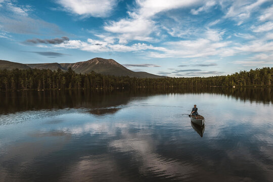Outdoorsy woman paddles boat alone on serene lake in Maine