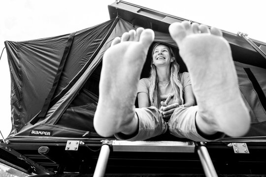 Woman with bare feet sits in roof top tent and laughs and smiles