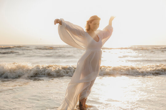 Woman dancing on the beach near the ocean at sunset