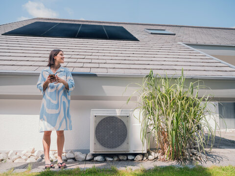 Woman with smartphone near thermal heat pump and solar panel at home