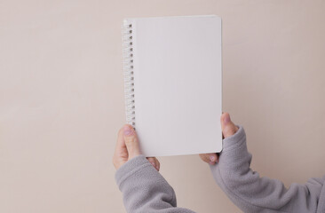 Wwoman's hands in a sports jacket hold a blank notebook on beige background.
