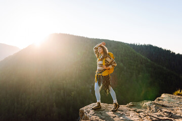Young hiker with yellow hiking backpack standing on cliff at sunset. Real view. Beautiful woman...