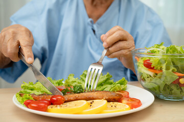 Asian elderly woman patient eating salmon stake and vegetable salad for healthy food in hospital.