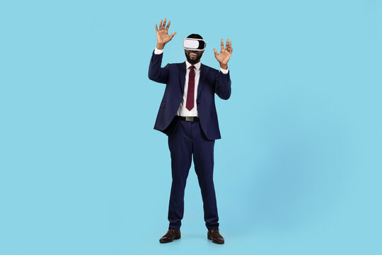 Excited Black Businessman In VR Headset Having Fun Over Blue Studio Background, Cheerful African American Male In Suit Enjoying Virtual Reality Experience, Using Modern Technologies For Leisure