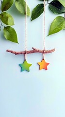 A rustic branch suspended by twine, adorned with two colorful star ornaments, set against a backdrop of lush green leaves and a soft blue sky.