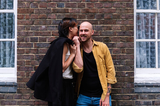 Young man whispering boyfriend's ear in front of building
