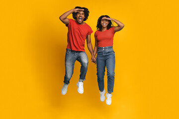 A happy couple leaps into the air, holding hands, with big smiles on their faces. They wear casual red shirts and jeans, creating a fun and energetic atmosphere.
