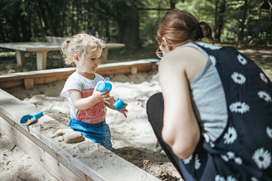 Mother playing with little daughter in sandbox on a playground