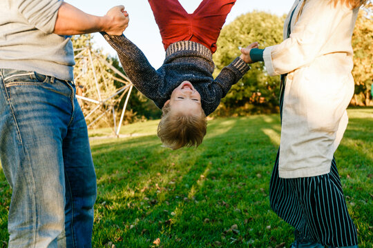 Parents holding cheerful boy upside down at park