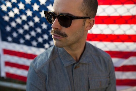 Young man with sunglasses in front of US-American flag on fence
