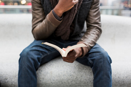 Young man sitting on bench reading a book, partial view
