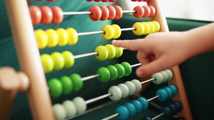 Close up of a childs hand counting colorful beads on a wooden abacus - Powered by Adobe