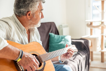 Senior man relaxing at home playing acoustic guitar