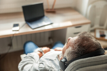 Elderly man relaxing listening music with headphones at home desk