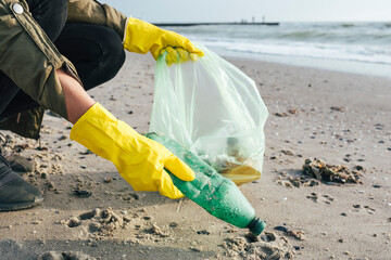 Hand's of environmentalist collecting plastic bottles in garbage bag at beach