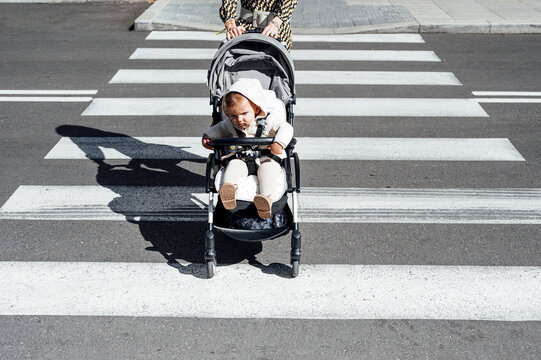 Mother with son in baby carriage crossing street in city on sunny day