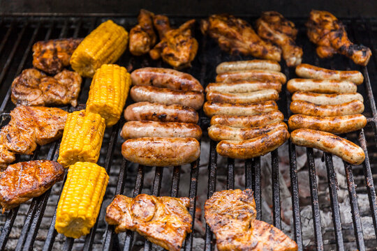 Different meat, maize and fried sausages on barbecue grill