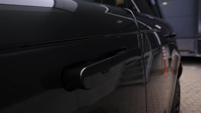 Close up of a Range Rover Autobiography side panel and handle in an indoor bay. Flush handle deploys, paint reflects posts and roller door with low key lighting.