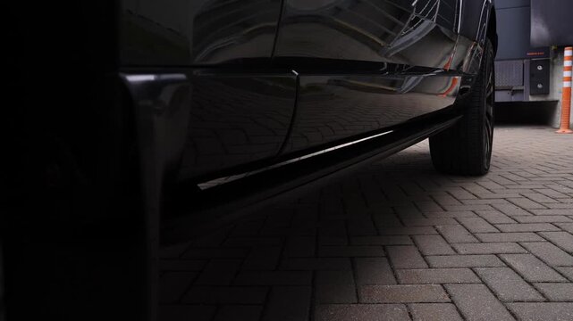 A low angle close up tracks a Range Rover step deploying at a loading bay with herringbone brick, an orange striped bollard, and a HORMANN dock unit in soft daylight.