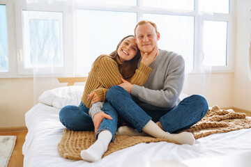 A young couple enjoys a warm embrace on a bed in a cozy room. A beautiful man and woman enjoy time together and relax on the bed. The concept of comfort and love.