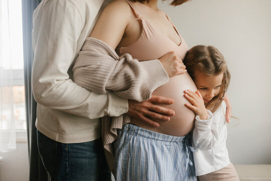 Girl embracing belly of pregnant mother at home