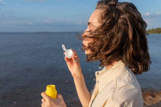 Woman blowing bubbles in front of sea at sunset