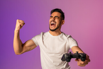 An overjoyed young Arab guy wins an online gaming competition. He plays with enthusiasm, shouting in excitement and making a triumphant YES gesture, surrounded by vivid neon lights.