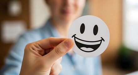 Person Holding a Smiley Face Sticker in a Bright Office Environment to Promote Positivity and Happiness