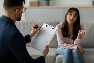 A woman sitting on a couch shares her feelings while speaking with a psychologist in an office setting. This therapy session focuses on her struggles with depression and mental health.