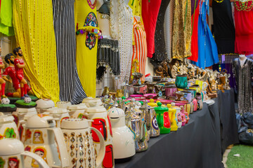 A vibrant market stall display of traditional Arabian coffee pots and colorful clothing at the...