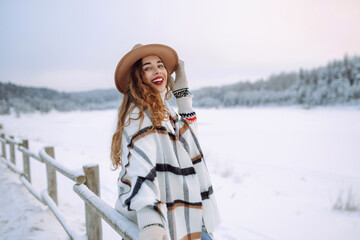 A woman in hat and wrapped in a scarf enjoys snowy day on a snow-covered lake. Beautiful woman...