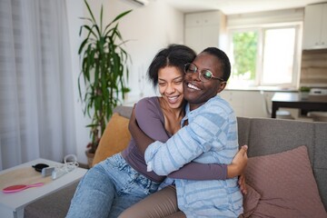 Two joyful friends hugging and laughing on the sofa at home