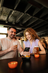 Couple enjoying drinks and looking at smartphone in pub