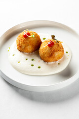 Crispy golden croquettes on a white plate with creamy sauce and garnish.