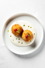 Crispy golden croquettes on a white plate with creamy sauce and garnish.