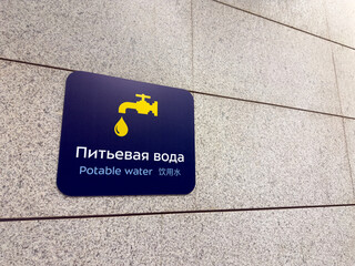 Sign on wall in three languages designating location for drinking fountain. Potable water sign at airport to care people waiting for their flights. Russian, English and Chinese text