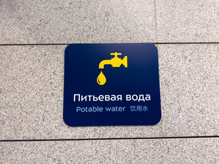 Potable Water sign on wall. Sign in Russian, English, and Chinese indicates the location of the drinking fountain at the airport. International interaction with multilingual signs