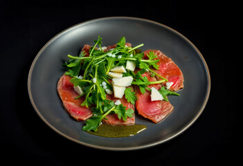 Beef Carpaccio with Arugula and Parmesan on Dark Plate