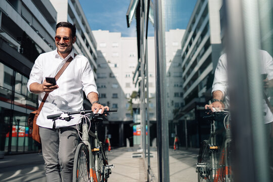 Businessman checking phone while pushing bicycle in city