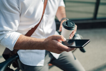 Businessman commuting, using smartphone holding coffee