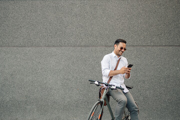 Smiling man on bicycle using smartphone outdoors