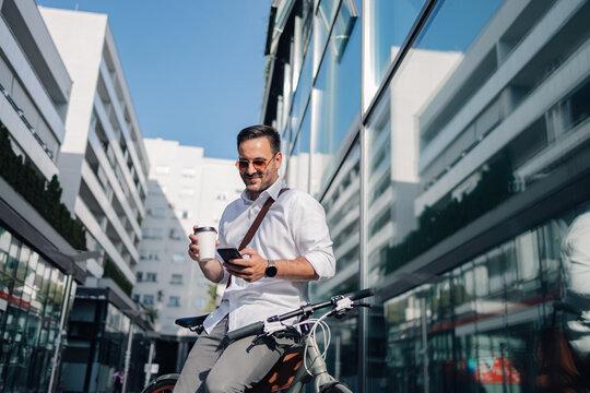 Businessman commuting by bicycle checking smartphone with coffee - Powered by Adobe